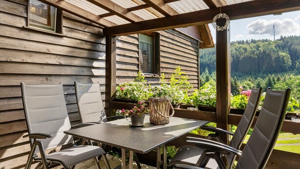 Une cabane en bois dotée d’un patio couvert, d’une table avec des chaises et offrant une vue sur une forêt.