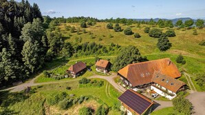 Vue aérienne d’une propriété rurale comprenant plusieurs bâtiments, un chemin sinueux et une végétation luxuriante.