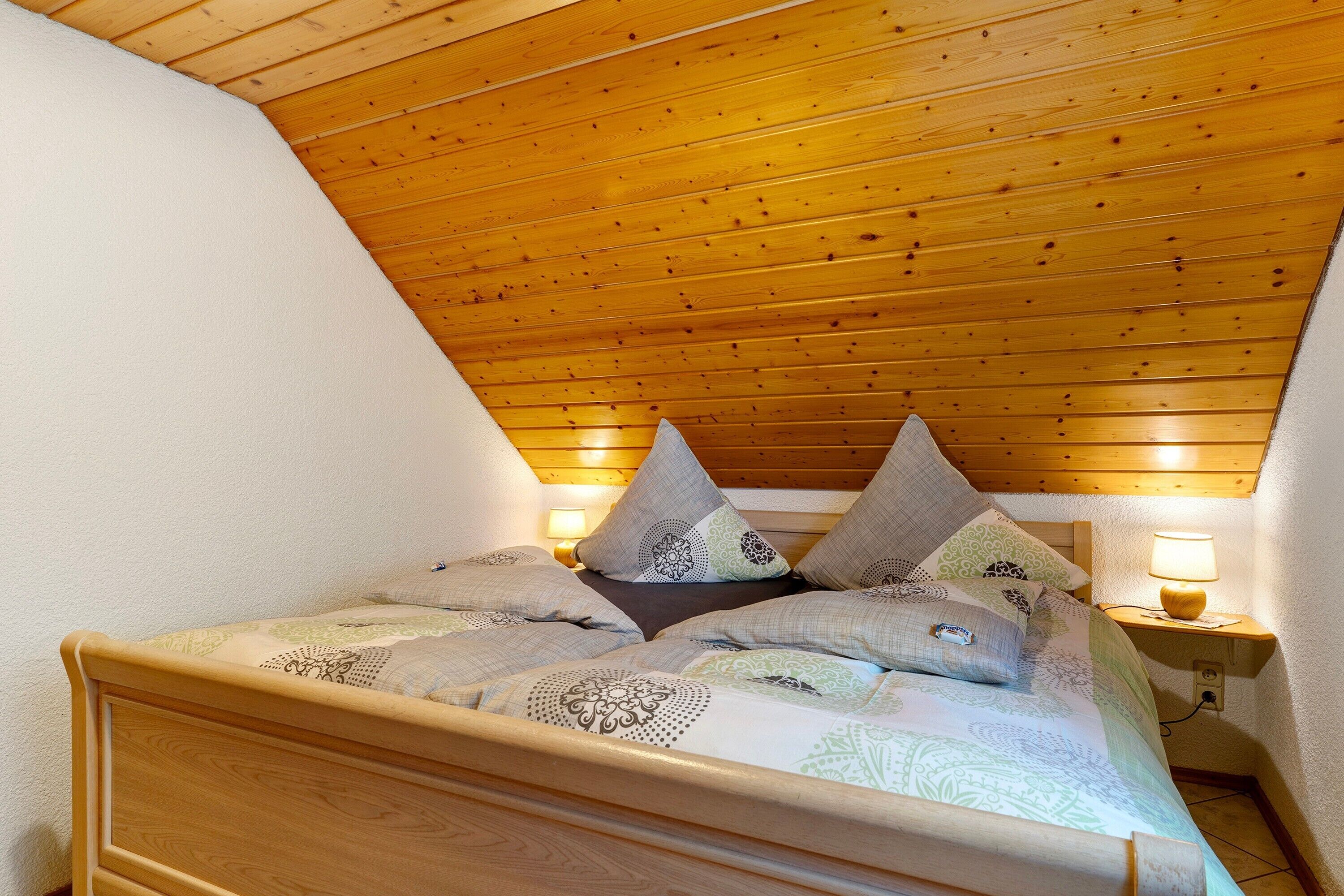 A bedroom with a wooden ceiling, a bed with patterned bedding, and two bedside lamps.