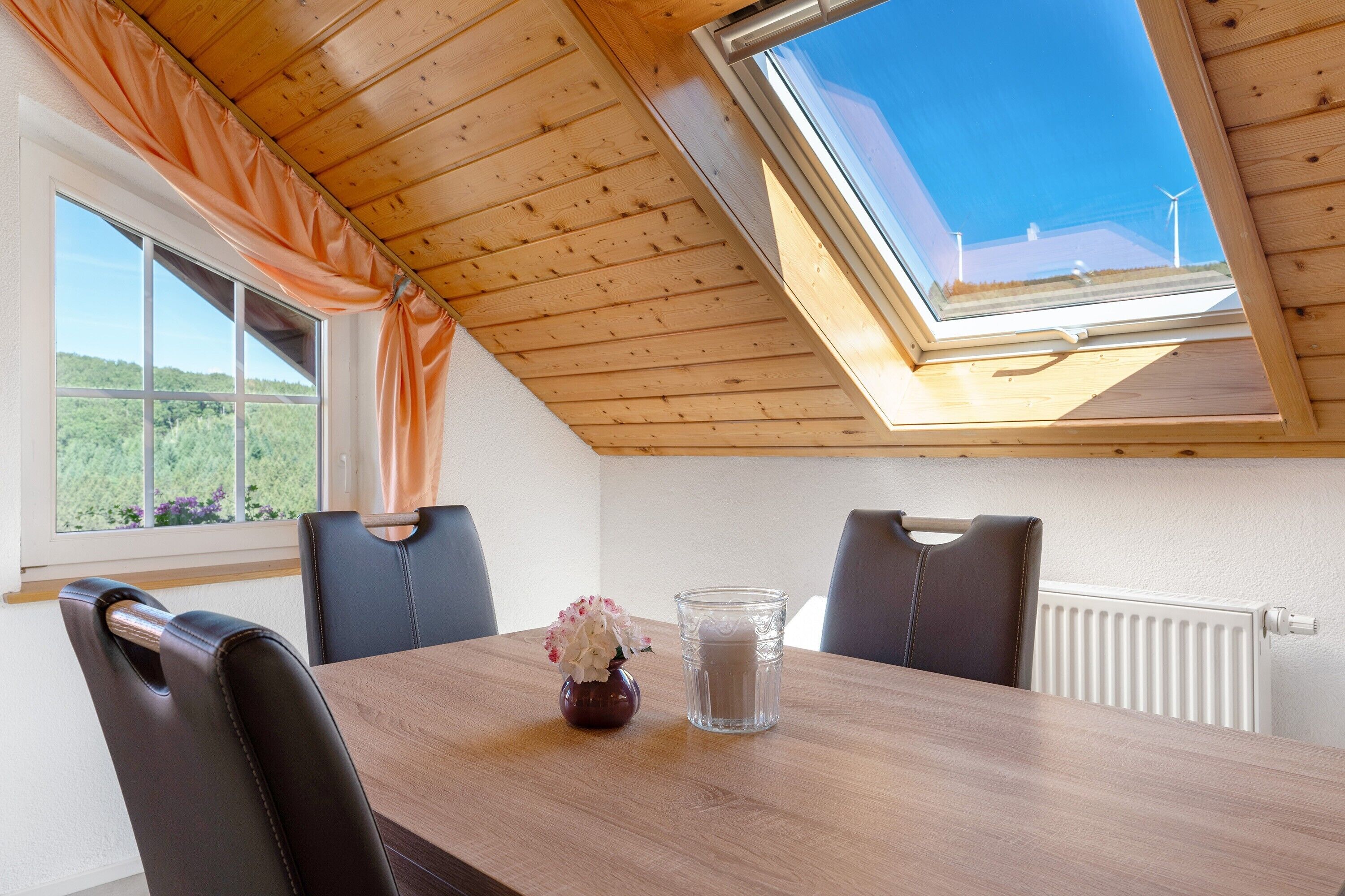 Un coin repas avec une table en bois, des chaises, un vase de fleurs et un verre.
