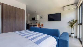 Une chambre d’hôtel moderne avec un grand lit, un canapé bleu, un téléviseur à écran plat et une plante en pot.