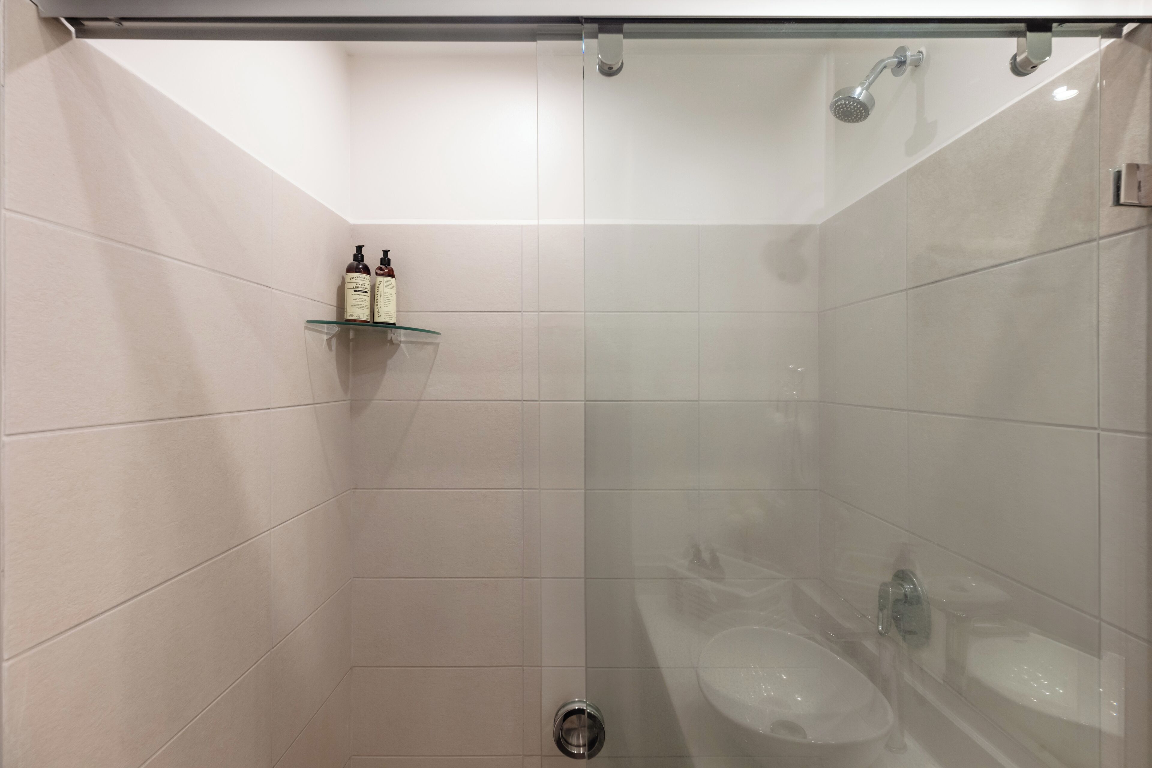Ein modernes Badezimmer mit Duschkabine aus Glas, einer Glasablage für Toilettenartikel und einem weißen Waschbecken.
