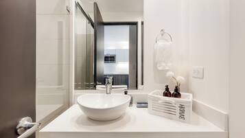 Ein modernes Badezimmer mit einem großen, weißen Waschbecken, einer Duschkabine aus Glas und Blick in die Küche.