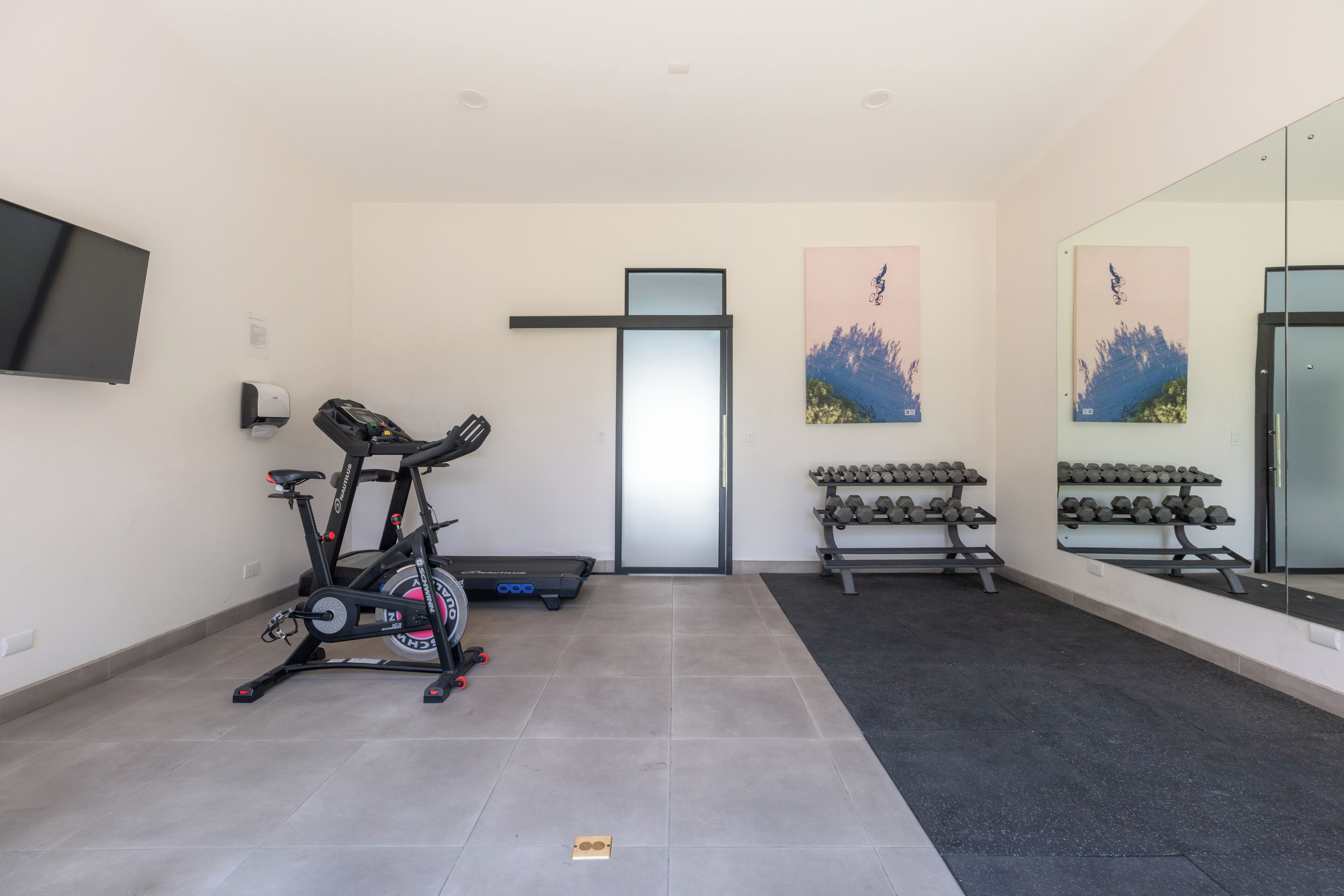 A modern gym with a stationary bike, dumbbells, and a large mirror.