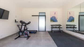 A modern gym with a stationary bike, dumbbells, and a large mirror.