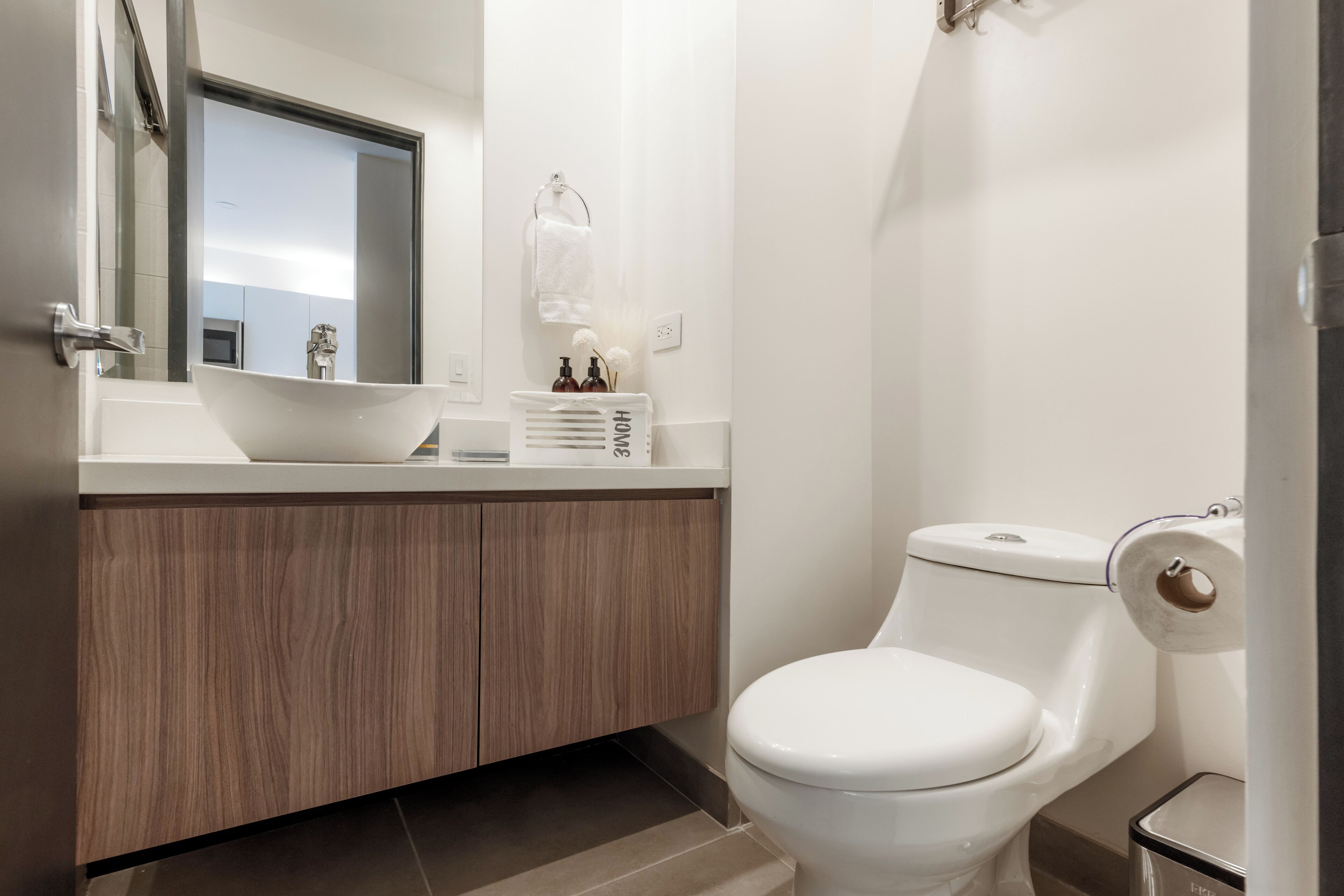 Un baño moderno con un lavamanos blanco, armarios de madera, un inodoro y un espejo.