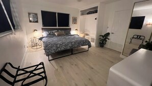 A bedroom with a bed, bedside tables, a chair, a wardrobe, and a door. - Newly renovated home near Hard Rock Stadium and major highways! (Miami Gardens)
