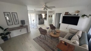 A modern living room with a sofa, coffee table, and chairs. There is a dining area with a table and chairs, and a kitchen in the background. - Newly renovated home near Hard Rock Stadium and major highways! (Miami Gardens)