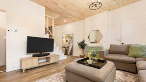 Ein modernes Wohnzimmer mit Flachbildfernseher, einer Couch, einem Couchtisch und einer Treppe, die zu einer oberen Etage führt.