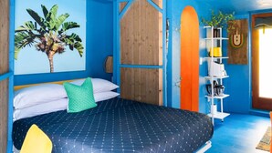 Ein Zimmer mit einem Bett, einer Holztür, einem Regal mit Gegenständen und einer Wand mit einer Pflanze.