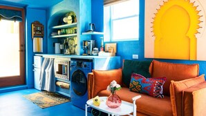 Ein kompakter Wohnraum mit Küchenzeile, einer Couch mit bunten Kissen und einer dekorativen Sonnenausschnitt an der Wand.