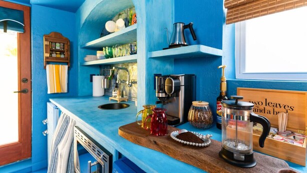 Eine Küche mit blauen Wänden, einer Holzausziehtafel, einer Kaffeemaschine, einem Wasserkocher und diversen Küchenutensilien.