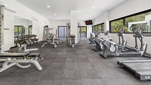 Ein modernes Fitnessstudio mit unterschiedlichen Trainingsgeräten, darunter Laufbänder und Kraftgeräte, und einem großen Fenster mit Blick ins Freie.