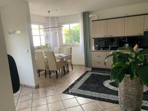 A modern kitchen with light-colored cabinets, a dining area with a table and chairs, and a large potted plant.