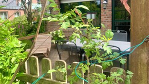 Ein Garten mit Holzzaun, einem Backsteinhaus und einem Tisch mit Stühlen.