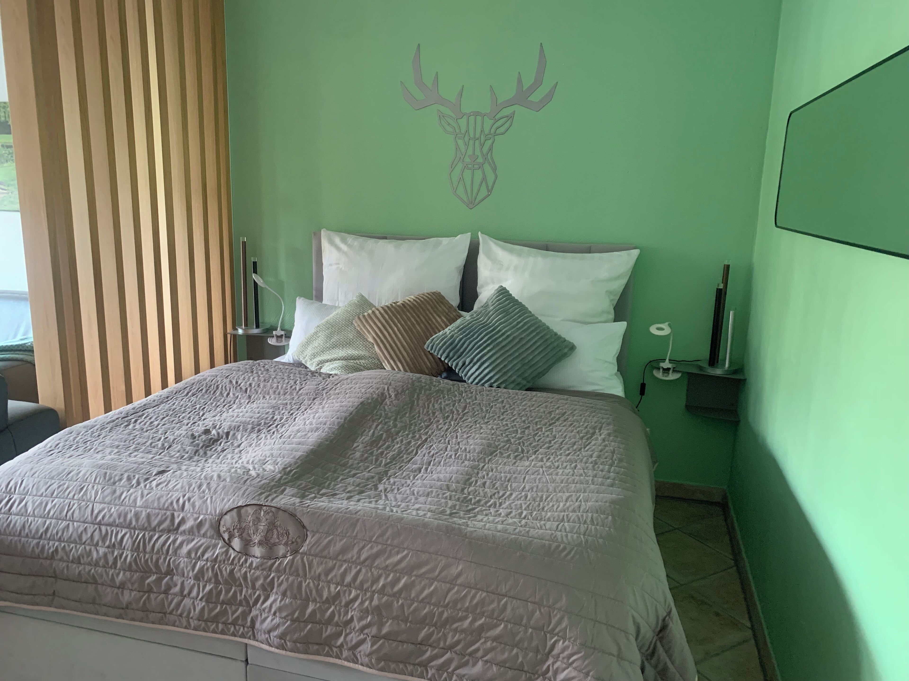 A neatly made bed with a quilted cover, a headboard with two pillows, and a wall-mounted deer head decoration.