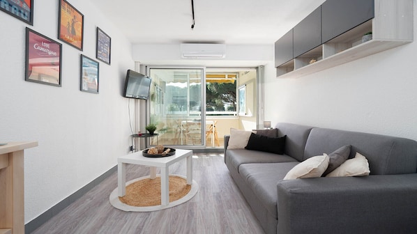 A modern living room with a grey sofa, a small white table, and a TV mounted on the wall.