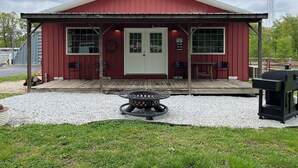 A red building with a white door, two windows, and a porch with chairs. - Tack Room @ Redemption Ranch: Grill, Deck, Peaceful, Unique, Comfortable (Marionville)