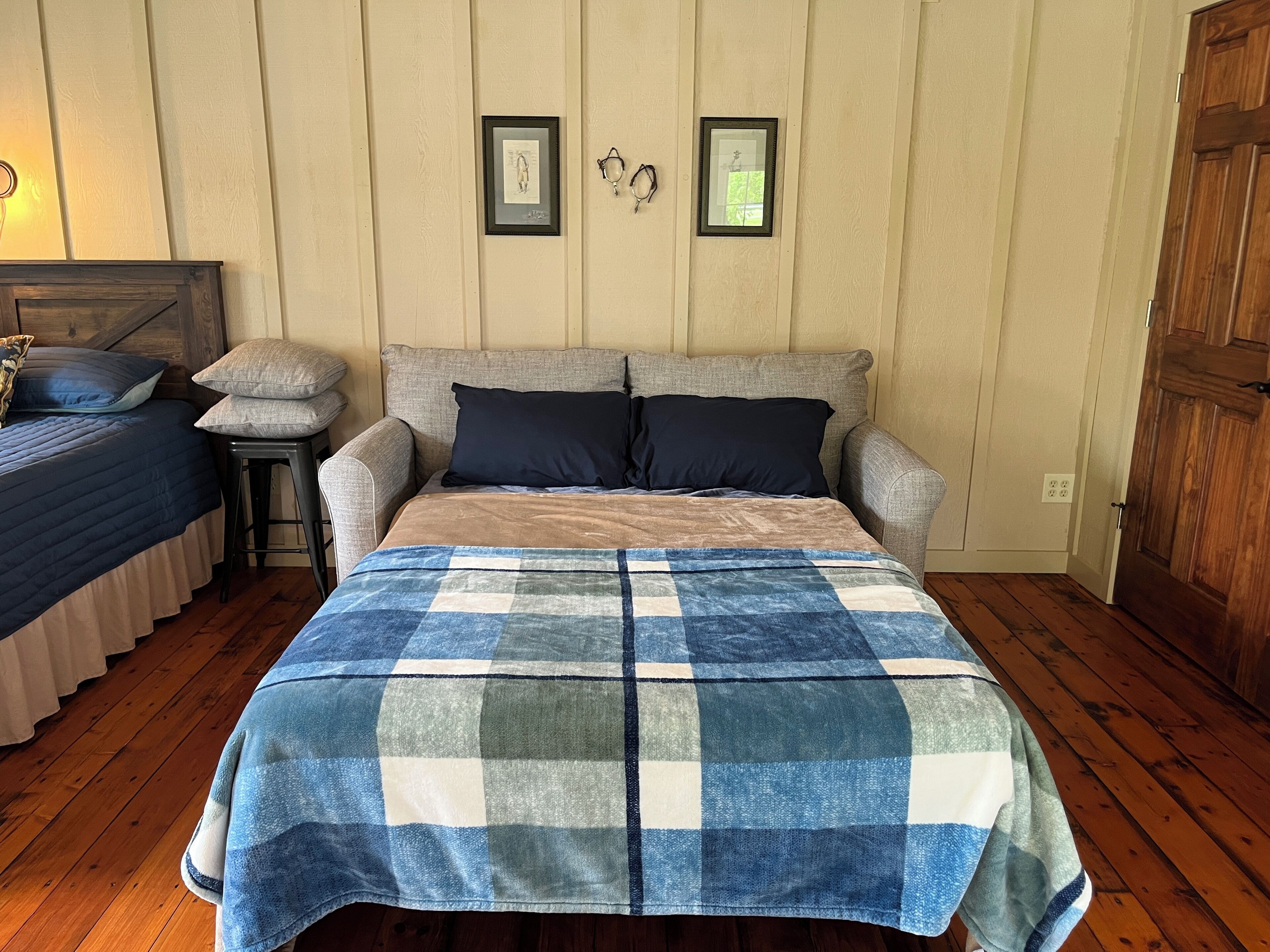 A bedroom with a large bed, two side tables, a wooden wardrobe, and a wall with two framed pictures.