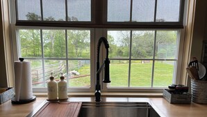 A kitchen with a stainless steel sink, a wooden cutting board, and a window overlooking a yard. - Tack Room @ Redemption Ranch: Grill, Deck, Peaceful, Unique, Comfortable (Marionville)