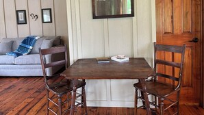 A wooden dining table with two chairs, a mirror, and a small stack of books on the table. - Tack Room @ Redemption Ranch: Grill, Deck, Peaceful, Unique, Comfortable (Marionville)