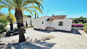 Un edificio bianco con tetto in tegole, vialetto in pietra e una palma.