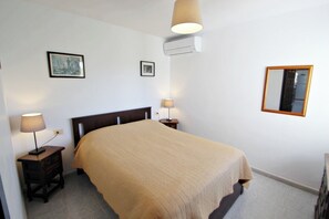 Une chambre à coucher comprenant un lit, deux tables de chevet avec des lampes, un climatiseur fixé au mur et deux tableaux encadrés.