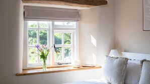 Ein Schlafzimmer mit Fenster, einem Bett, einer Lampe und einer Blumenvase.