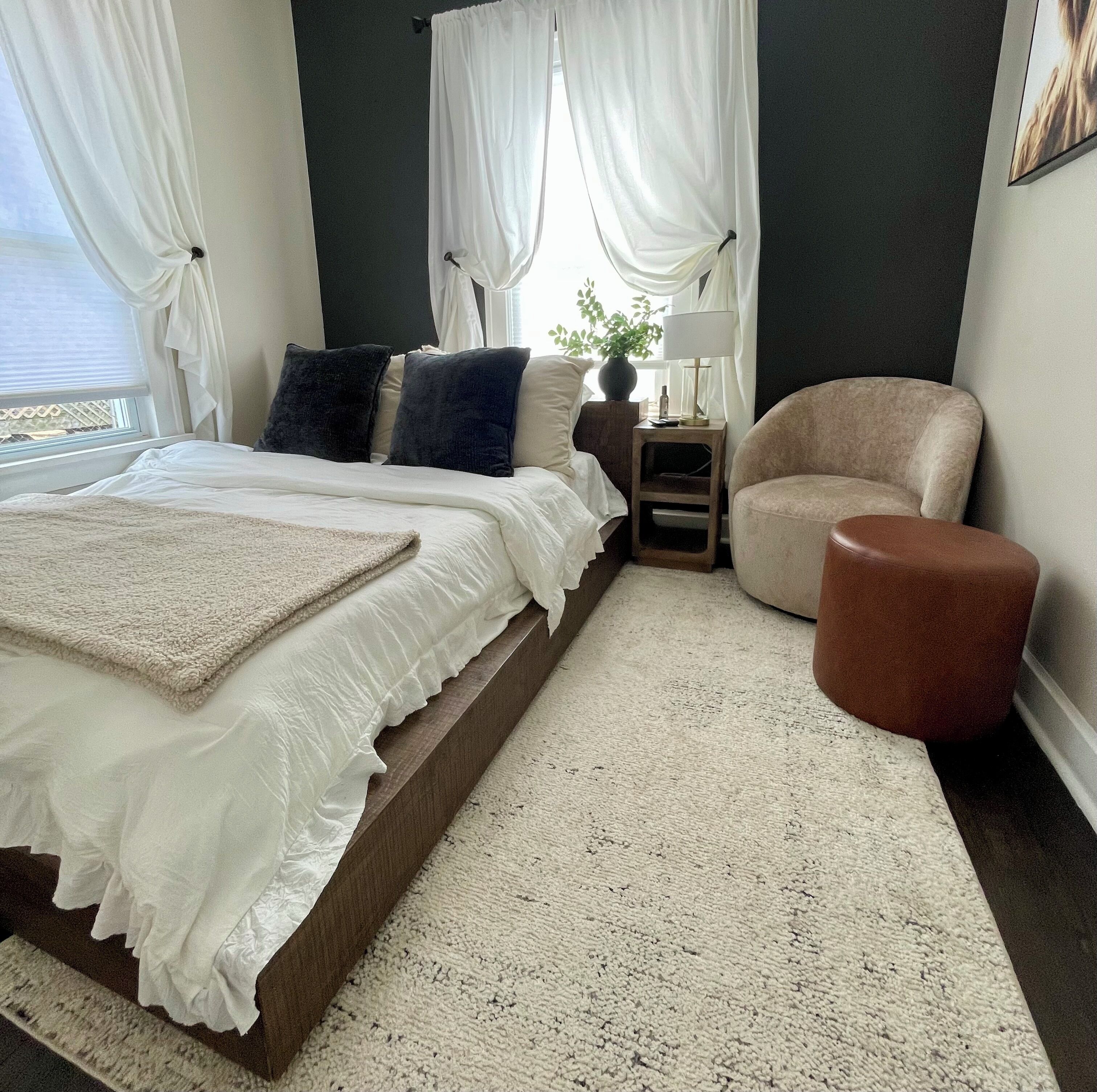 A bedroom with a bed, a nightstand, a chair, and a window with curtains.