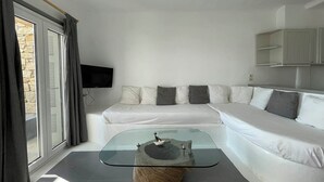 A modern living room with a glass coffee table, a white sofa, and a stone wall. - Apartment with Pool & Shared Infinity Pool, Sea View,  Pool Bar, Gym (C965+8J Mykonos, Řecko)
