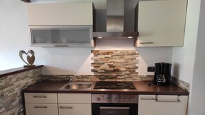 Una cocina compacta con horno integrado, cocina, lavamanos y cafetera.