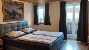 Un dormitorio con una cama grande, una mesita de noche con lámpara, un cuadro en la pared y vistas al exterior.
