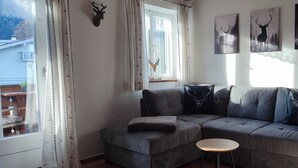 Una sala de estar con un sofá seccional gris, una pequeña mesa redonda y tres piezas de arte temático de ciervos.