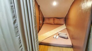 A corner bedroom with a bed, pillows, and a small table with items on it. - Aashvi Cozy Cabin (Lapu-Lapu)