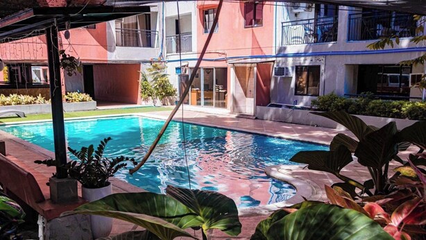 A swimming pool surrounded by tropical plants and a multi-story building with balconies. - Aashvi Cozy Cabin (Lapu-Lapu)