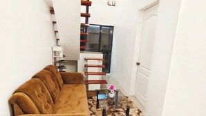 A living room with a brown sofa, a glass coffee table, and a patterned rug. - Aashvi Cozy Cabin (Lapu-Lapu)