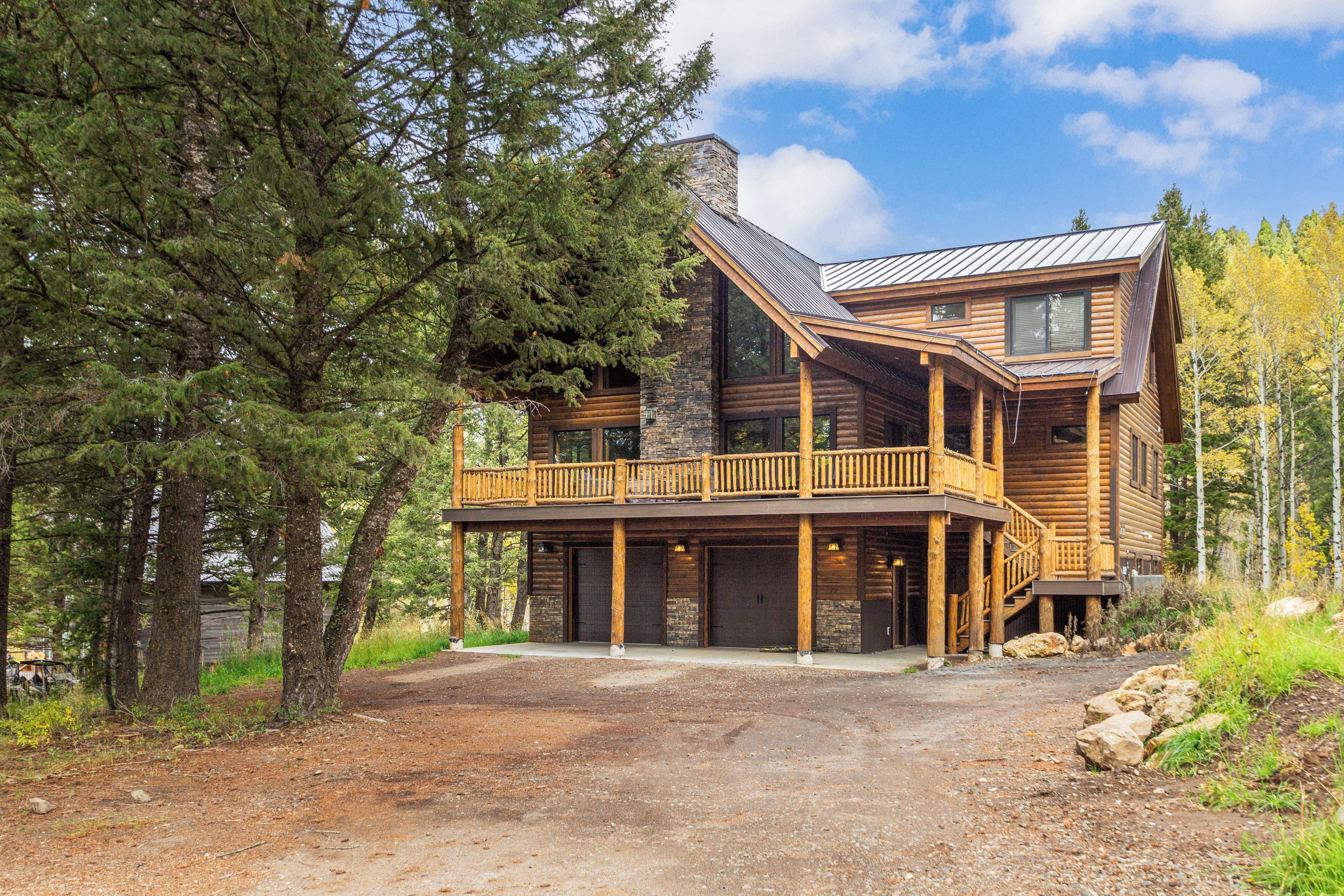 A log cabin with a balcony, a stone fireplace, and a covered porch.