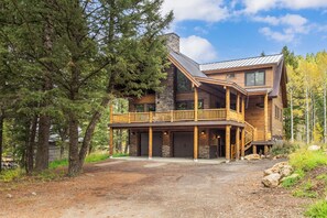 A log cabin with a balcony, a stone fireplace, and a covered porch.