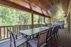 A covered deck with a table and chairs, a grill, and a hot tub.