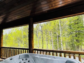 Eine Holzblockhütte mit Whirlpool und Blick auf einen Wald.