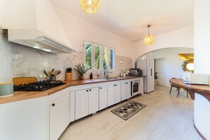 Une cuisine moderne avec des meubles blancs, un dosseret en marbre, une cuisinière à gaz et des luminaires suspendus.