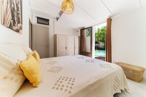 A bedroom with a bed, a wardrobe, a hanging light fixture, and a view of the outdoors.