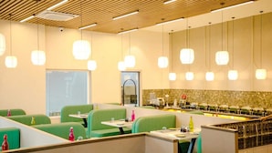 A modern restaurant with green booths, a counter with food displays, and pendant lighting. - Narayani Executive (Tuljapur)