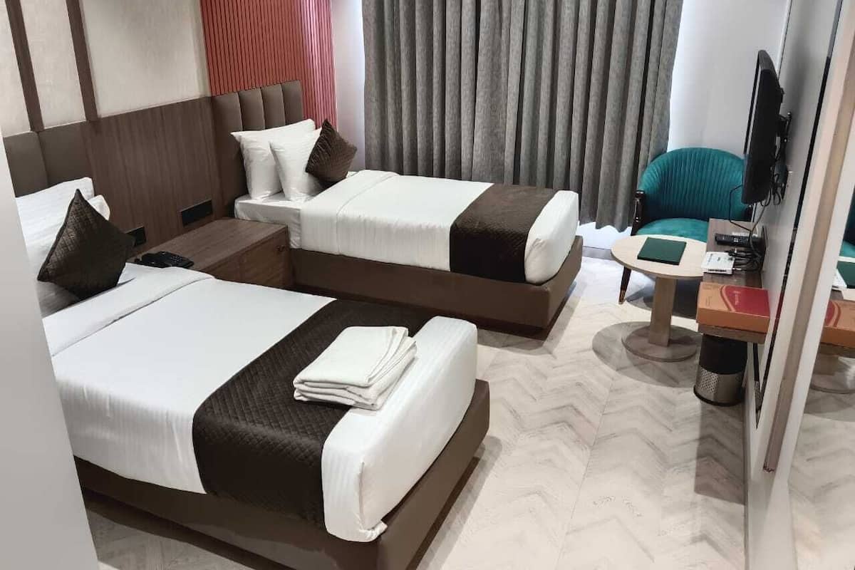A hotel room with two beds, a desk, a chair, and a television.