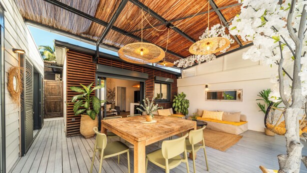A wooden deck with a dining table and chairs, surrounded by potted plants and a hanging chair. - Villa Latrille - Ermitage les bains - near the beach  (Saint-Paul)