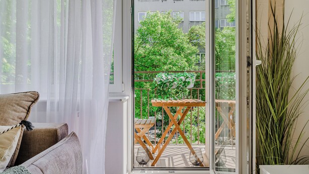A room with a sliding glass door leading to a balcony with a wooden table and chairs. - Lumina 4-room apart near Pałac Kultury (Warsaw)