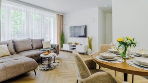 A modern living room with a sofa, dining table set for a meal, and a TV mounted on the wall. - Lumina 4-room apart near Pałac Kultury (Warsaw)