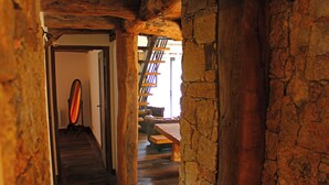 Un escalier en bois, avec un mur en pierre d’un côté, mène à une pièce dont le sol est également en bois. On y trouve un banc et une table.