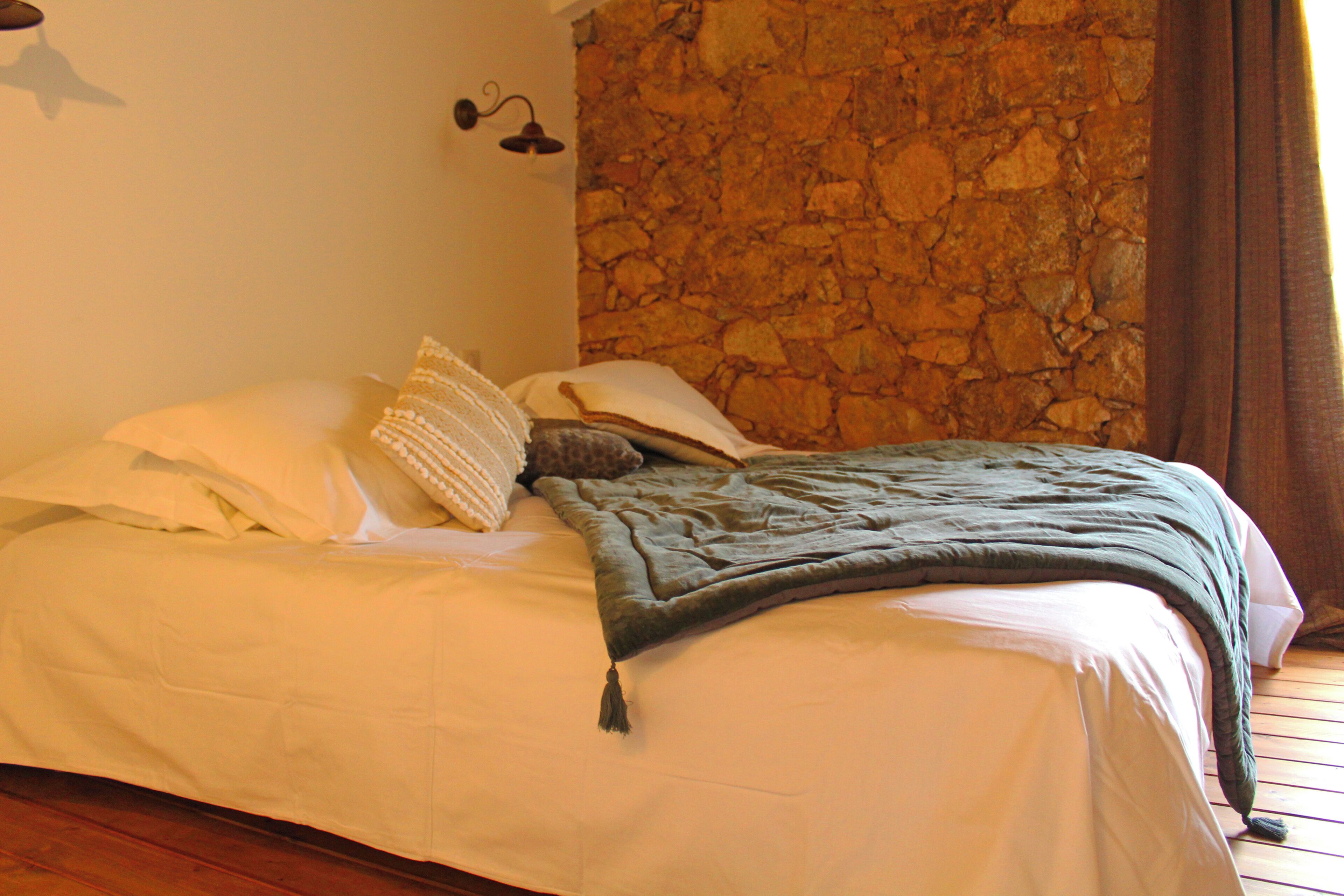 Ein Bett mit weißer Bettwäsche, einer grünen Decke und einer Steinwand im Hintergrund.
