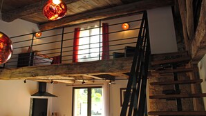 Un intérieur rustique avec des poutres apparentes, un étage supérieur en mezzanine agrémenté de rideaux rouges et un escalier.